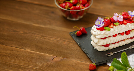 Pavlova dessert with strawberries and violet flowers as a decor on a wooden background. Place for text