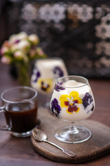 Dessert in a glass with fresh pansy flowers inside on a wooden background