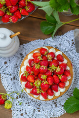 Honey cake with strawberries and cream cheese lying on the background of a plate with berries and a jar of honey on a wooden background