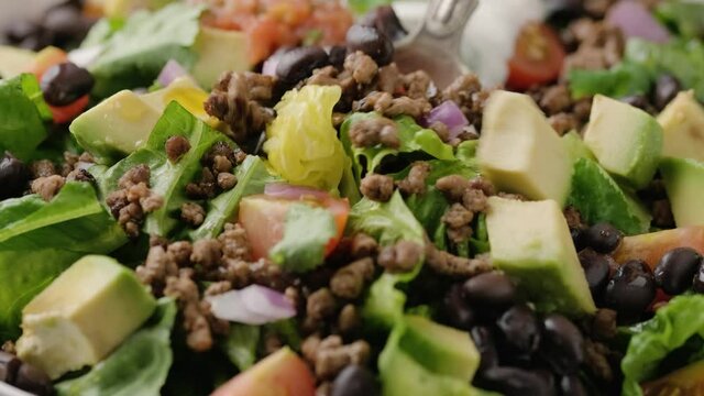 Picking Beef Taco salad with romaine lettuce, avocado, tomato salsa, black bean, using a tablespoon.