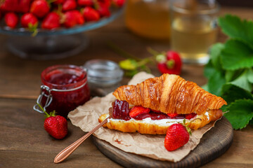 Croissant stuffed with curd cheese, strawberries and strawberry jam lying on a wooden board
