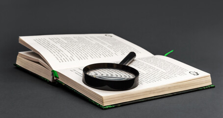 Magnifying glass with opened book on black. - 452685713