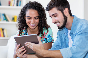 Laughing latin american couple watching movie with tablet computer