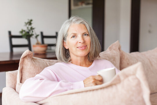 Portrait happy healthy middle aged woman sitting on comfortable couch at home
