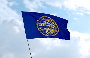 Flag of Nebraska in front of blue sky, realistic 3D rendering