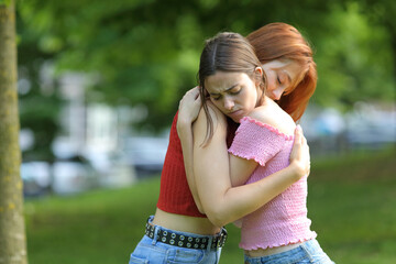 Sad women reconciling hugging in a park