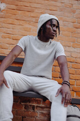 Portrait stylish African man in white clothes sitting on bench street style