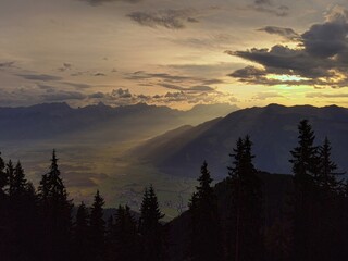 beautiful light in the morning on the mountains, with view of the alps in the background, tree silhouettes in the foreground and sunbeams in the middle