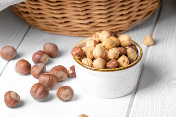 Peeled hazelnuts in a bowl and whole hazelnuts on a white wooden background, close up. Healthy snack and healthy eating, fall forest harvesting
