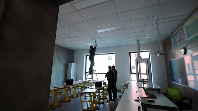 Silhouette of three workers adjusting fire safety in the room. Repair and inspection of fire sensors in rooms.