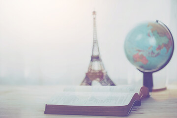 open bible with small world globe and small Eiffel tower on wooden table, window light. Christian background, bible study, or world mission ministry concept with copy space