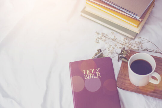 The Holy Bible  and a cup of black coffee over blurred book stack on the bed, Christian background morning devotional concept with copy space