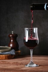 Pouring red wine into a glass on wooden table with dark background