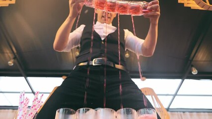 The bartender pours cocktails into many glasses at once. Bartenders show.