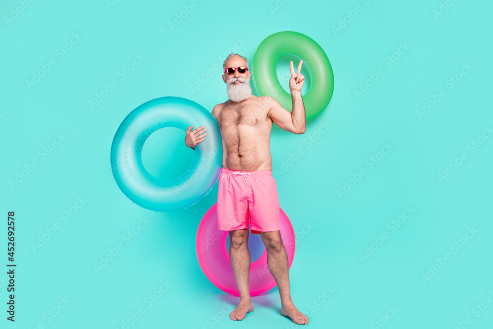 Poster photo of friendly man hold lifebuoy show v-sign posing wear sunglass pink shorts isolated teal color