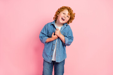 Photo of grateful adorable ginger little boy hold hands wear denim jacket isolated pink color background