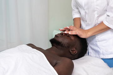 Fototapeta premium woman masseur doing a face and head massage to black man