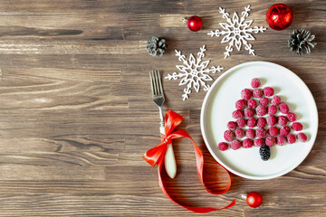 Funny Christmas tree shaped sweet fresh raspberry berry on plate on wooden background for kids children breakfast. xmas food with new year decorations with copy space