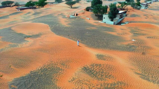 Aerial Panning Shot Of Man Standing On Sandy Landscape During Landscape, Drone Flying On Sunny Day - Al Madam, UAE