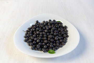 ripe chokeberry in bowl on white background