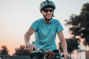 Hombre joven paseando con una bicicleta en la carretera junto a la puesta de sol con gafas de ciclismo