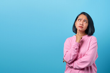 Attractive asian woman thinking and looking up empty space on blue background