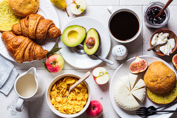 Breakfast table with cornflakes, croissants, fruit, cheese and cup of coffee. Gray tile background, top view.