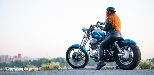 Fototapeta na wymiar Rear view of red-haired curly woman in helmet on motorcycle outdoors.