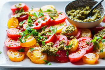 Red and yellow tomatoes salad with pesto sauce on gray plate. Italian cuisine concept.