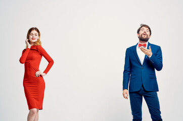 a man in a suit next to a woman in a red dress communication fashion light background