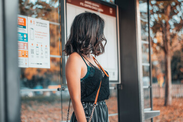 Muchacha joven de pelo oscuro esperando en la parada del autobús de pie para realizar el recorrido
