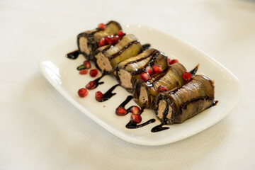 Fried stuffed eggplant with cheese and meat, tomatoes and sauce on white plate, selective focus