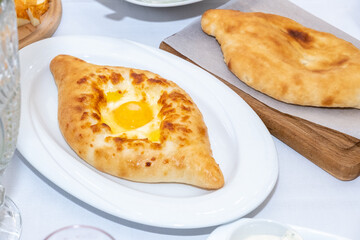 Adjara-style khachapuri, baked dough with egg, cheese and pieces of butter on white plate, selective focus