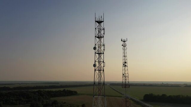 Drone camera moves around the telecommunication towers. The sun shines through the silhouette of the tower