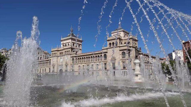  Ca&ntilde;os de la fuente en la plaza Jos&eacute; Zorrilla de Valladolid creando arco iris y con la academia de caballer&iacute;a de fondo, Espa&ntilde;a