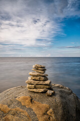 meditative rock cairn on top of a boulder with long exposure ocean and sky in the background