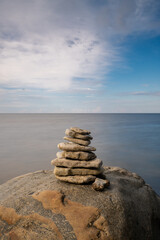 meditative rock cairn on top of a boulder with long exposure ocean and sky in the background