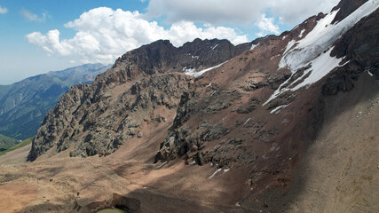 High rocky mountains are sometimes covered with ice and snow. A huge glacier passes between the peaks. The ice is gradually melting. The stones are lying on glacier. Steep cliffs. The view from drone