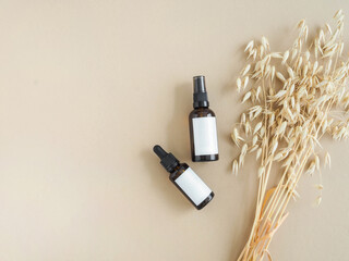 Two amber bottles with white labels and bouquet of dry oats on beige background.