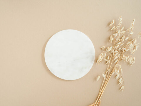 Marble white round podium and bouquet of dry oats on beige background.