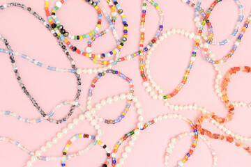Necklaces and bracelets made from multicolored beads and pearls on a pink pastel background. - obrazy, fototapety, plakaty