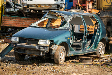 Damaged green car waiting in a wreck yard to be recycled