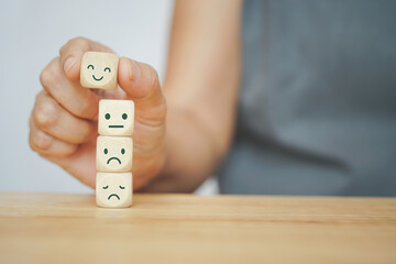 senior human hand selected happy face wood cube and others on green background for customer service...