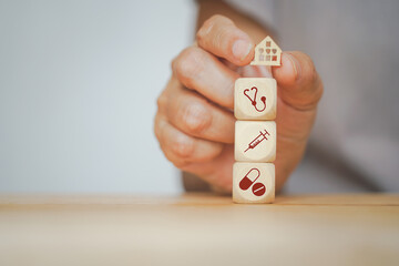 senior human hand holding mini wood house and medical icon on wooden cubes for annual health checking, health and medical, family health insurance, wellness, wellbeing concept