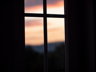 Close-up silhouette window with blurred sunset as background. The middle of the window looks like a cross.