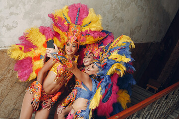 Woman in brazilian samba carnival costume with colorful feathers plumage with mobile phone take...