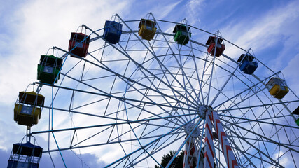 Fototapeta premium Colorful ferris wheels in the amusement park on a background of blue sky with clouds. Toned image. Bottom view.