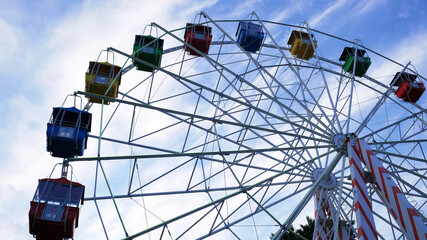 Colorful ferris wheels in the amusement park on a background of blue sky with clouds. Toned image. Bottom view.