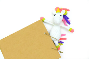 Mock up brown clear empty blank craft paper bag with funny crochet toy of a white unicorn. White background