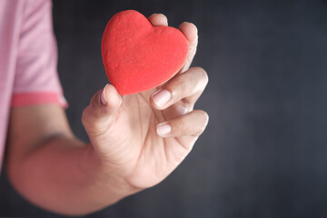 Fototapeta premium man holding red heart against black background 